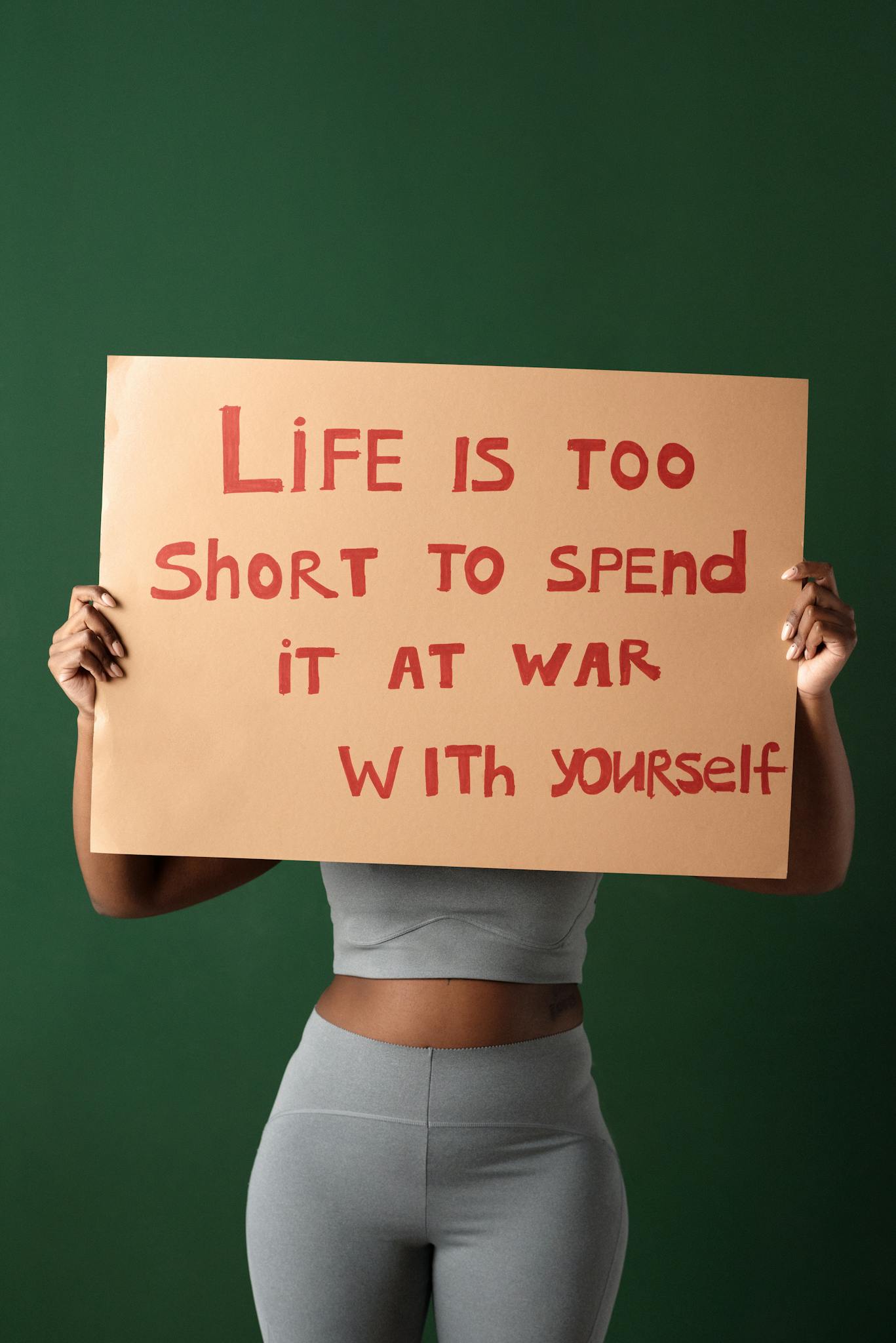 Woman holding motivational sign about self-love and peace on green background.